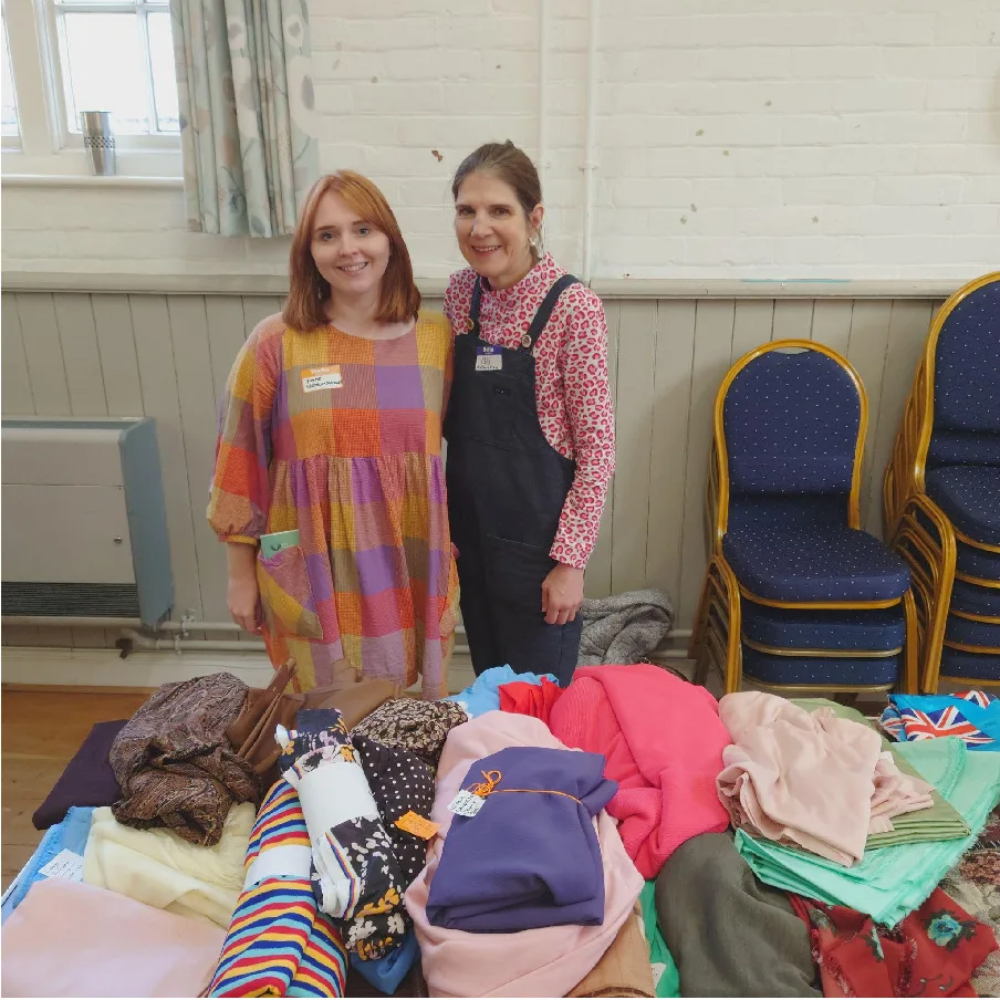 Yvette and Mel standing behind tables of fabric at the Surrey Sews sewing swap in November 2023